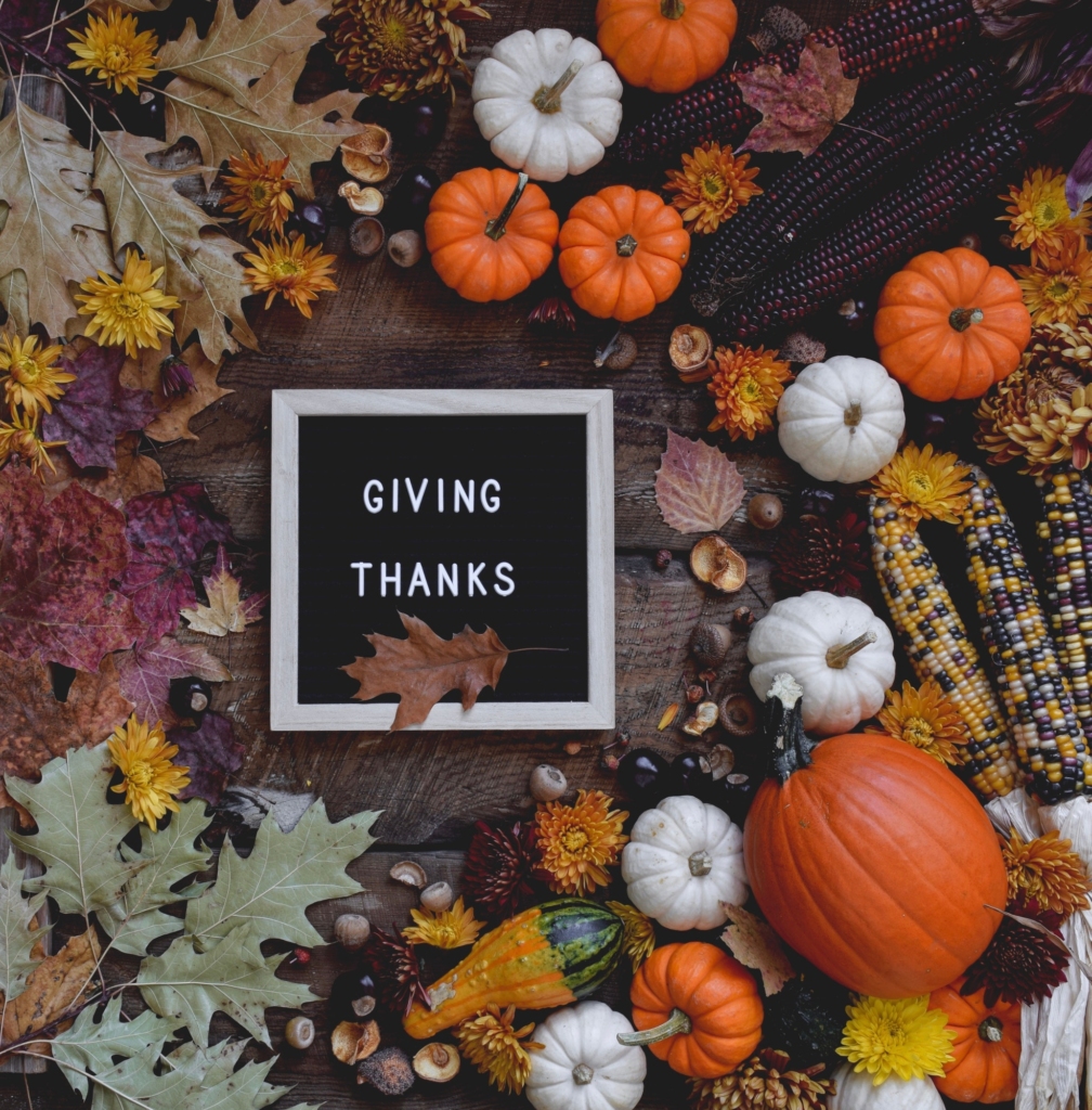 Letter board saying Giving Thanks surrounded by fall leaves, mini pumpkins, corn and gourds